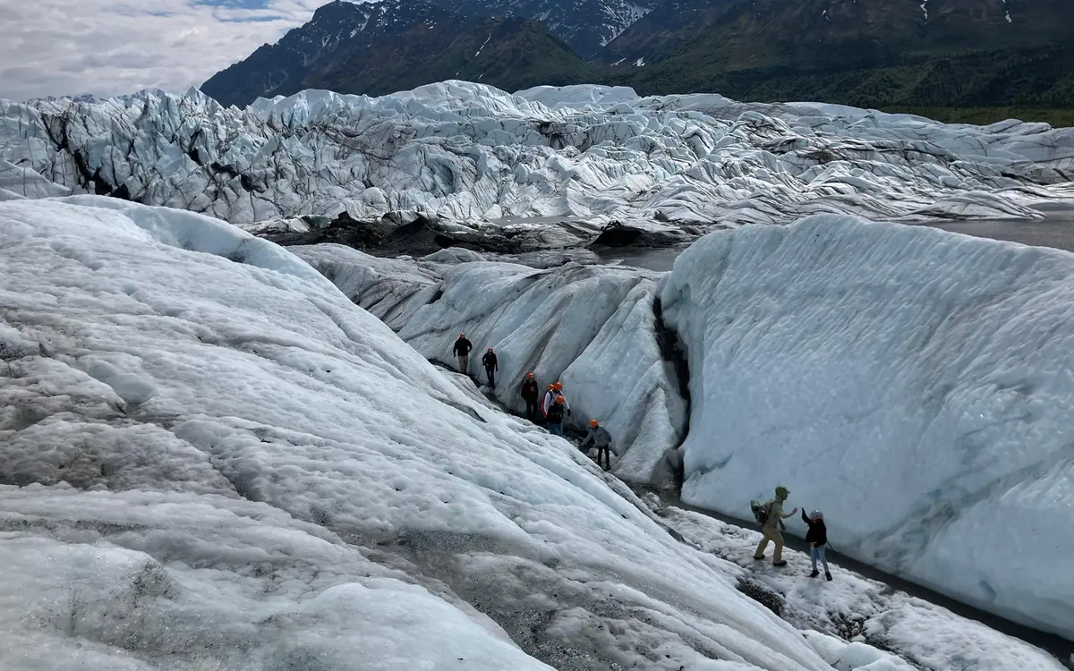 A guide in a helmet leading a small group across the Matanuska Glacier in Alaska