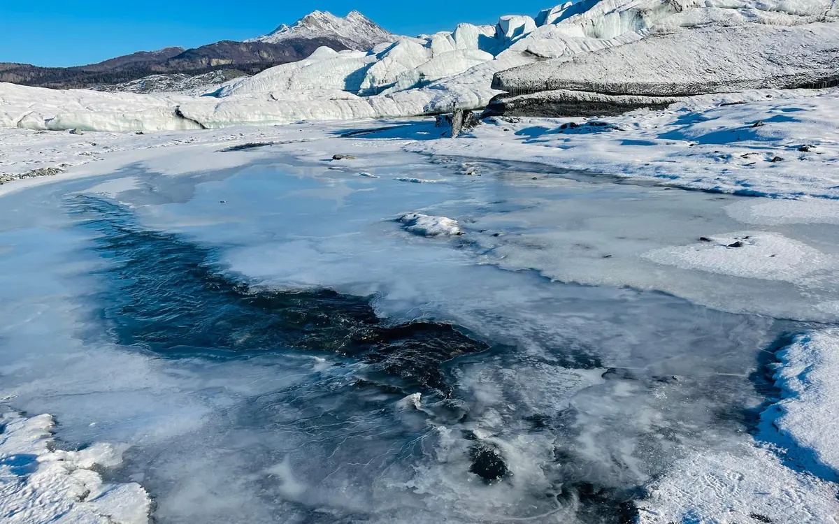 A guide and a small mixed-age group in helmets and cleats on gentle ice at the Matanuska Glacier